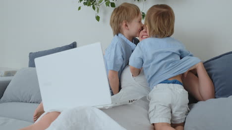 Mama-Sitzt-Mit-Einem-Laptop-Auf-Der-Couch.-Zwei-Jungenkinder-Singen-Und-Küssen-Ihre-Mutter.-Glückliche-Familie,-Liebevolle-Kinder